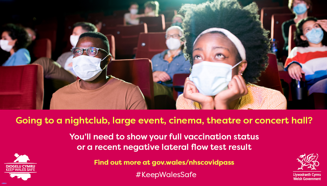 a photo of two people watching a film at a cinema and wearing masks