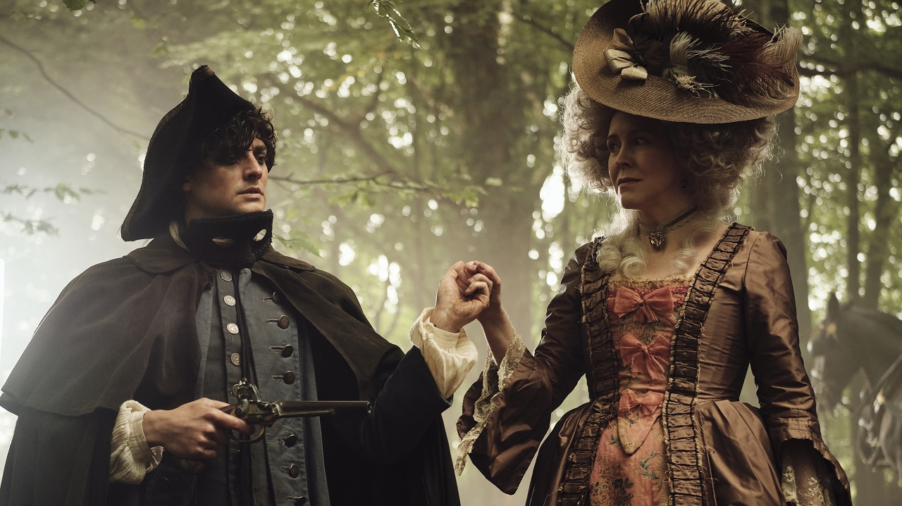 still from timestalker featuring aneurin barnard and alice lowe lowe wearing georgian costumes and standing in a forest. They are holding hands while barnard (left) holds an old pistol.