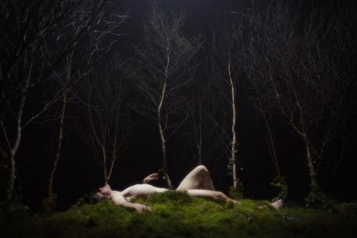 still from nant featuring a nude person lying on their back in a dark forest