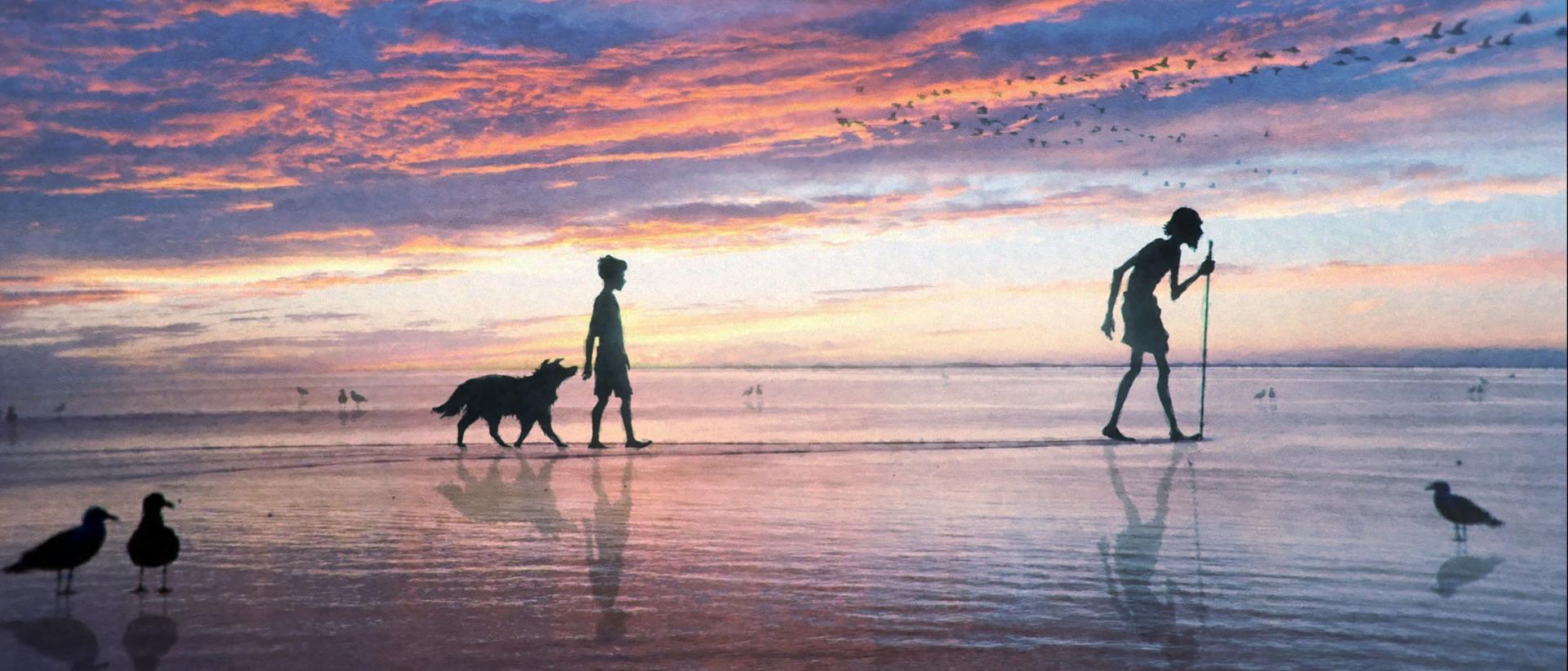 a man, a boy and his dog walk across a beach