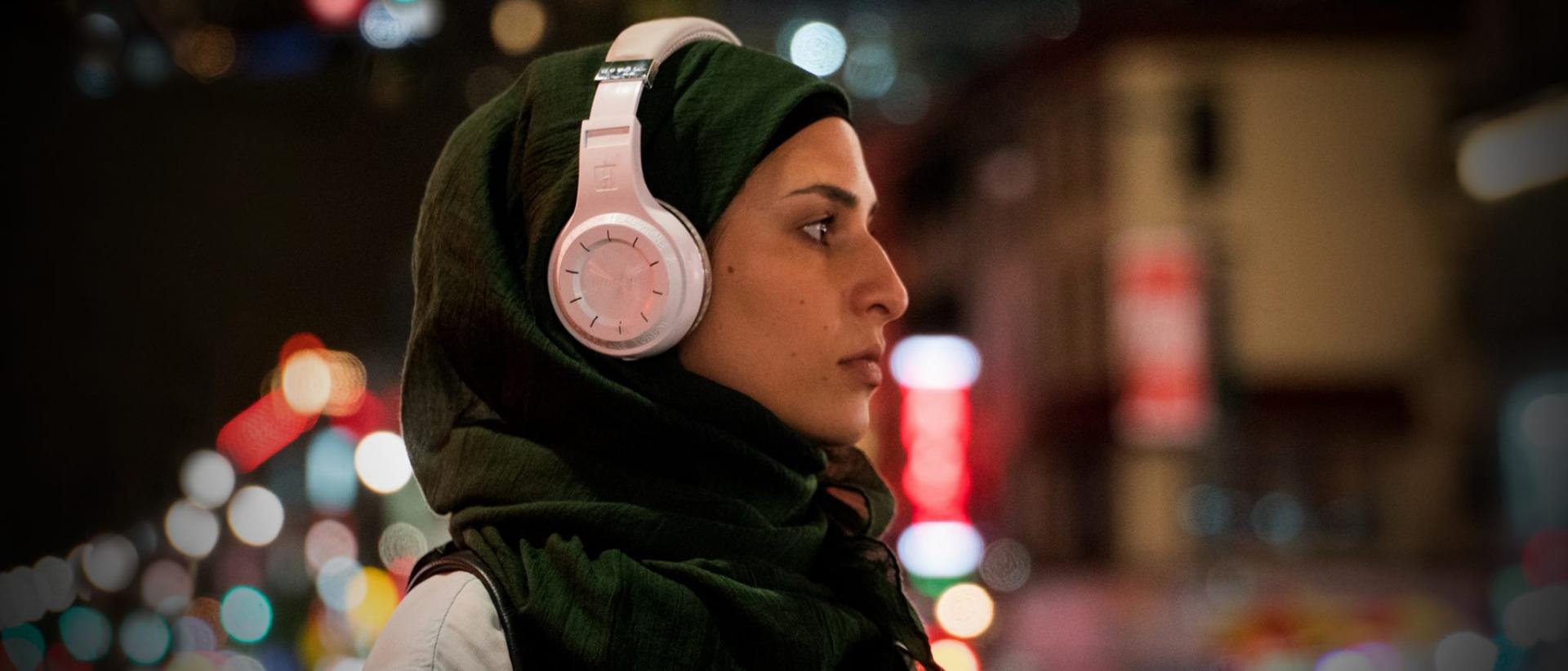 a young woman wearing a hijab and headphones walks through New York at night