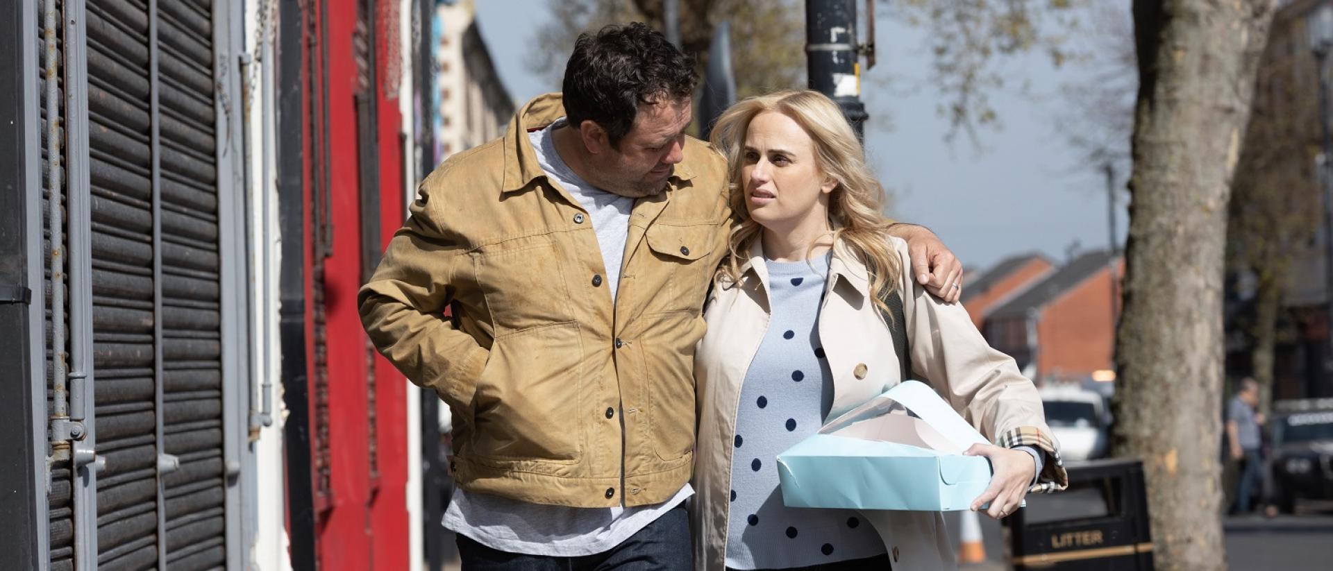 A still from The Almond and The Seahorse featuring Celyn Jones and Rebel Wilson walking down a street during the day. He has his arm around her shoulders, and she is carrying a box.