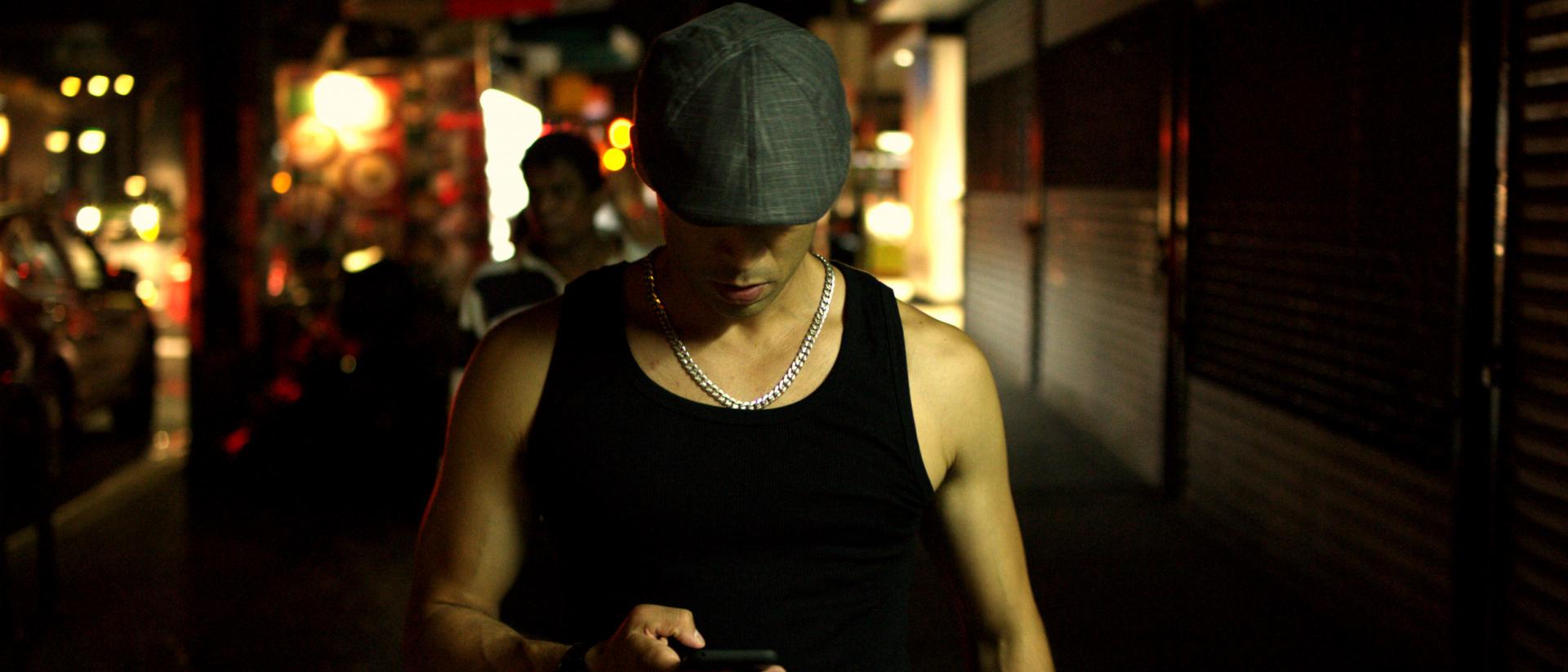 a person wearing a black vest and a grey flatcap looking down at their phone