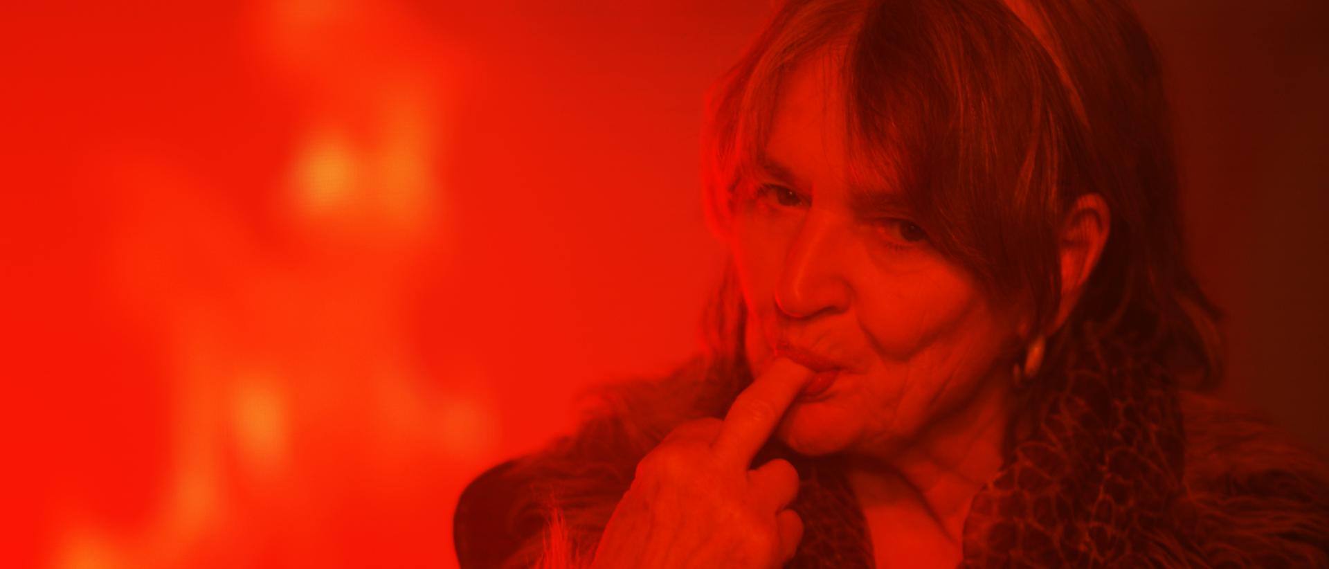 a woman under red light with the end of her middle finger in her mouth,