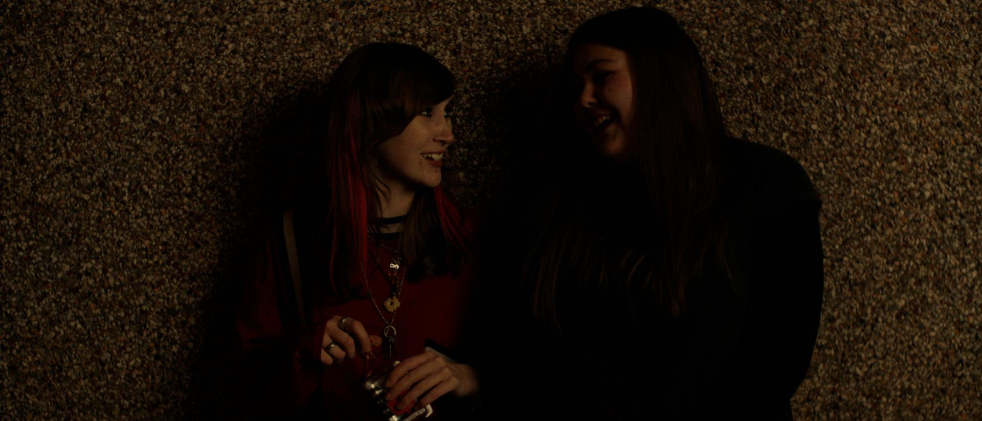 two young women standing against a wall and laughing at each other
