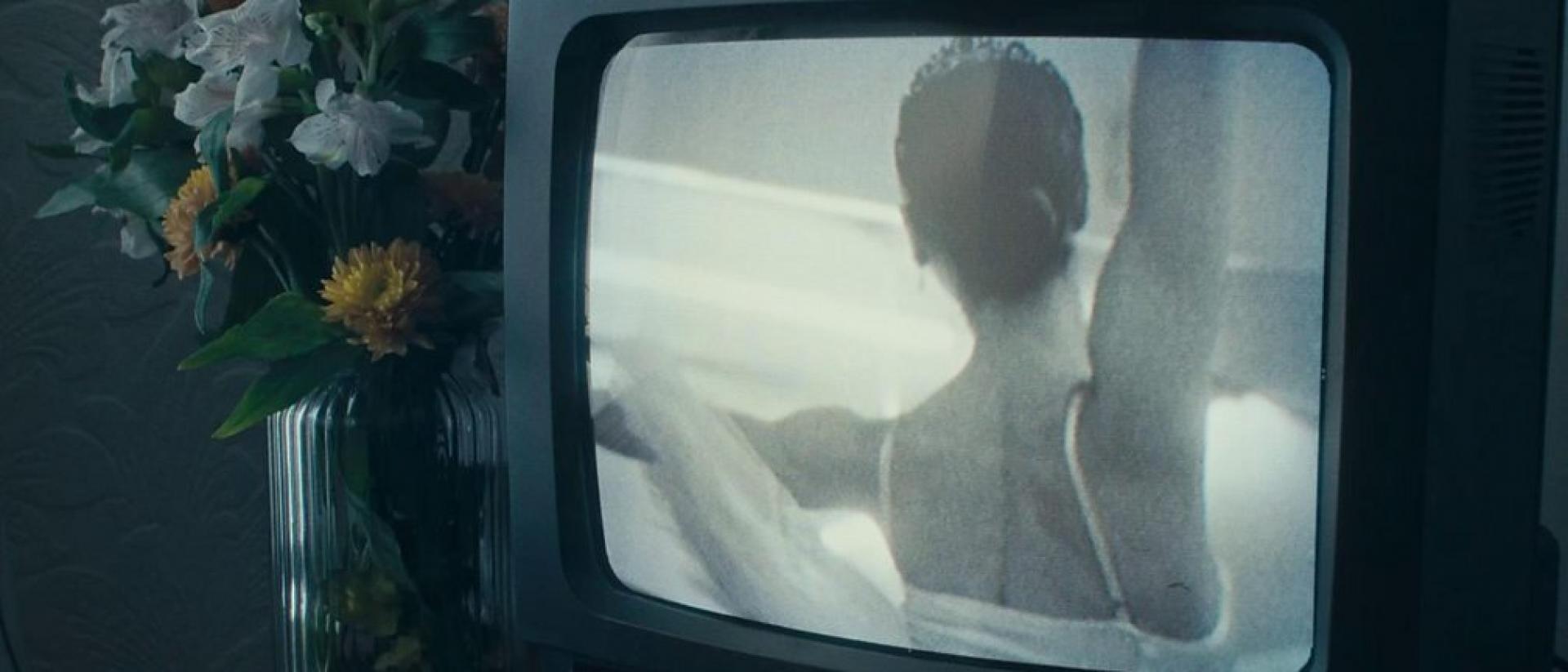 Still from Yew featuring a vase of flowers next to an old television showing a ballet dancer from behind.