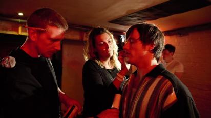 a costume assistant and hair and make up assistant work on an actor on a film set