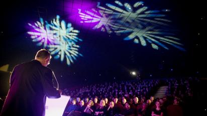 a photo of the iris prize awards ceremony featuring a person on stage talking to a crowded cinema. There are white light patterns projected on the ceiling.