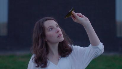 a still from Gwledd / The Feast featuring Annes Elwy holding a piece of broken wine bottle up to the light to look through it