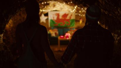 two people standing in a dark cave looking at a welsh flag on the wall illuminated by fairy lights