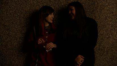 two young women standing against a wall and laughing at each other