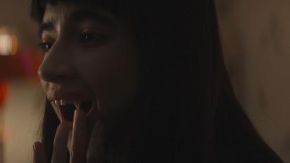 Still from Humanist Vampire Seeking Consenting Suicidal Adult featuring a vampire with long dark hair carefuly touching their fingertip to their long sharp canine tooth.