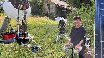 photo of a person sitting on an outdoor film set, with grass and camera equipment around them