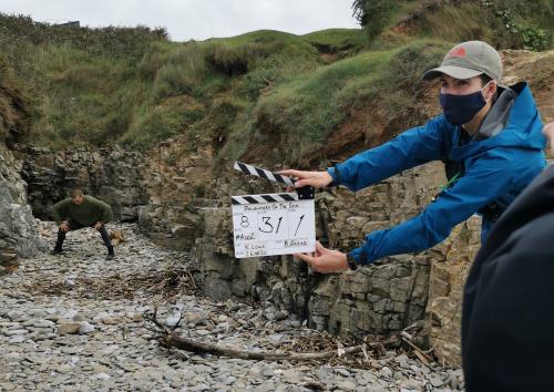 film crew on set holding a clapperboard and wearing a mask