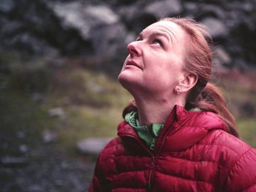 w person wearing a red coat standing in an old slate quarry and looking up at a cliff