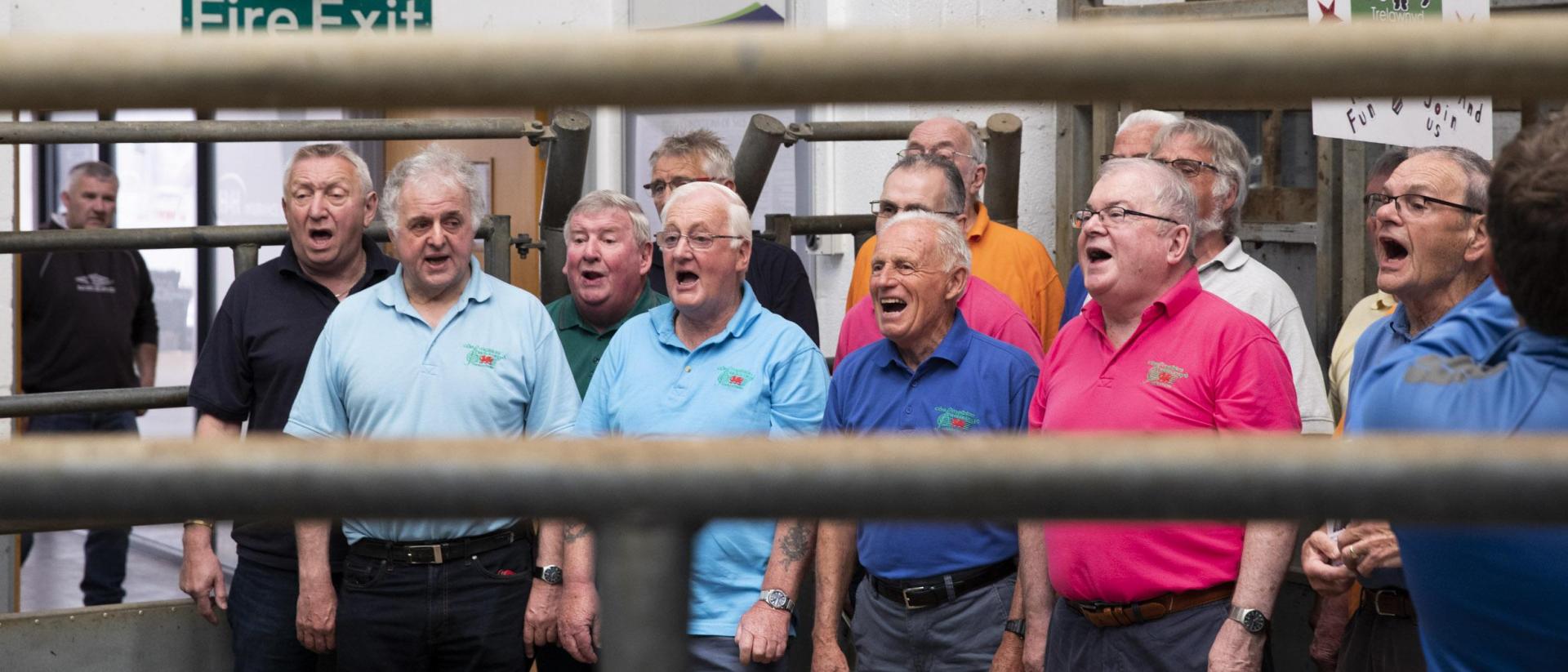 a still from men who sing featuring a male voice choir singing in a hall