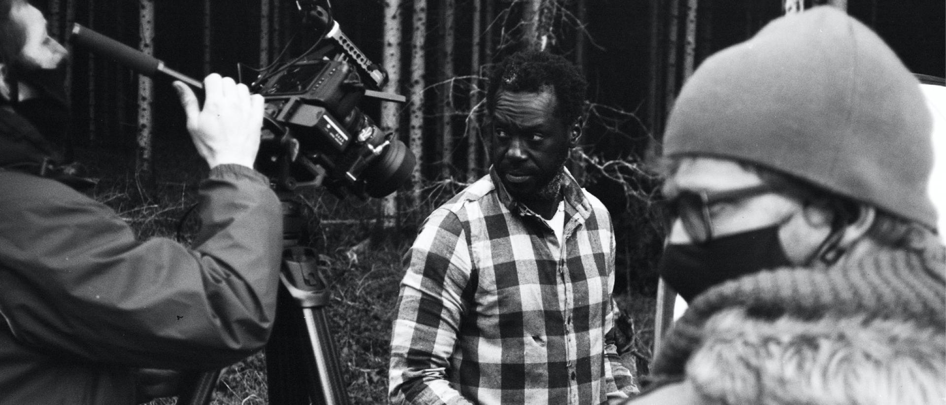 a black and white photo of three people making a film in a wooded area