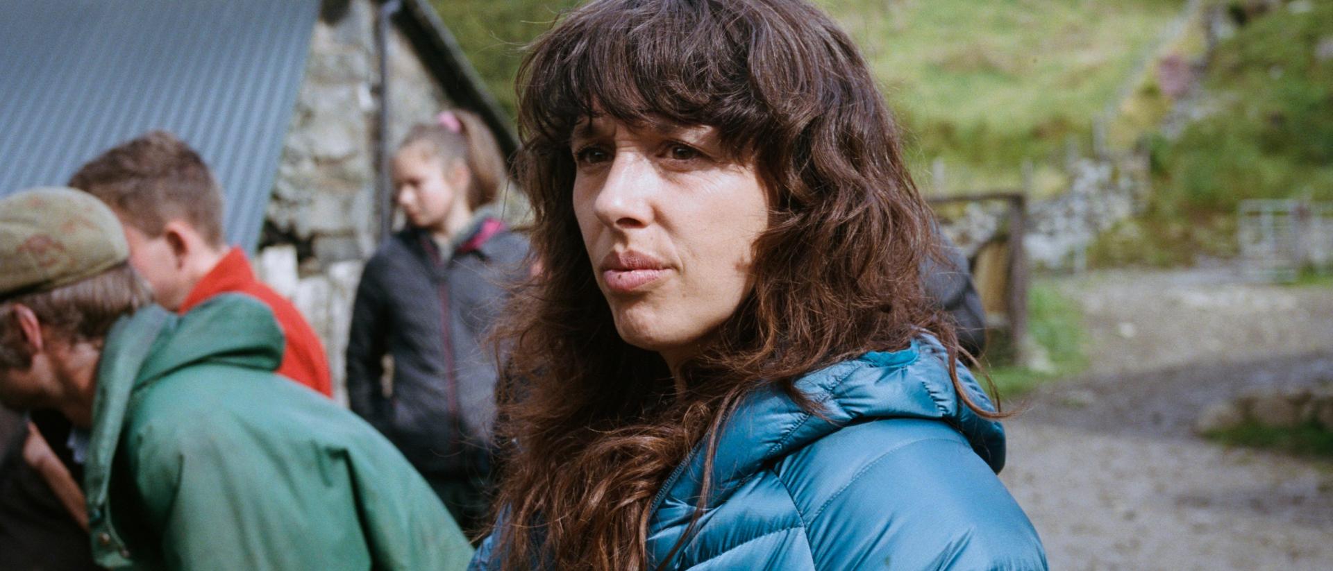 a person wearing a thick blue coat standing in a farmyard with three people behind her