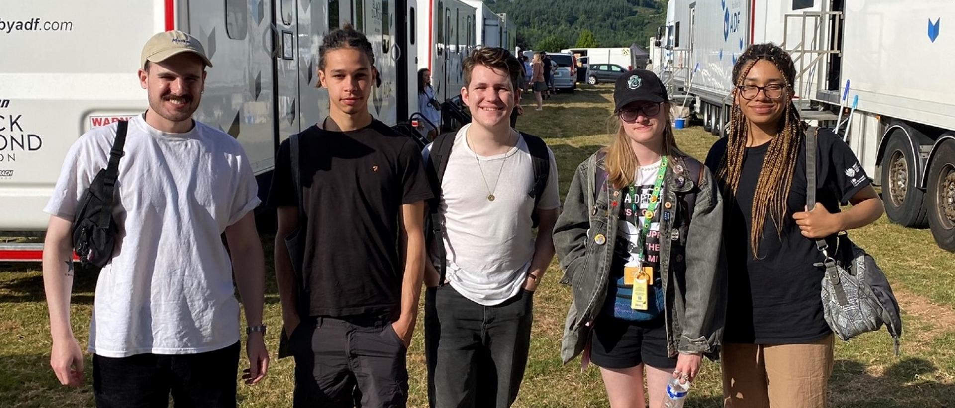 five people posing for a photo in between film trucks