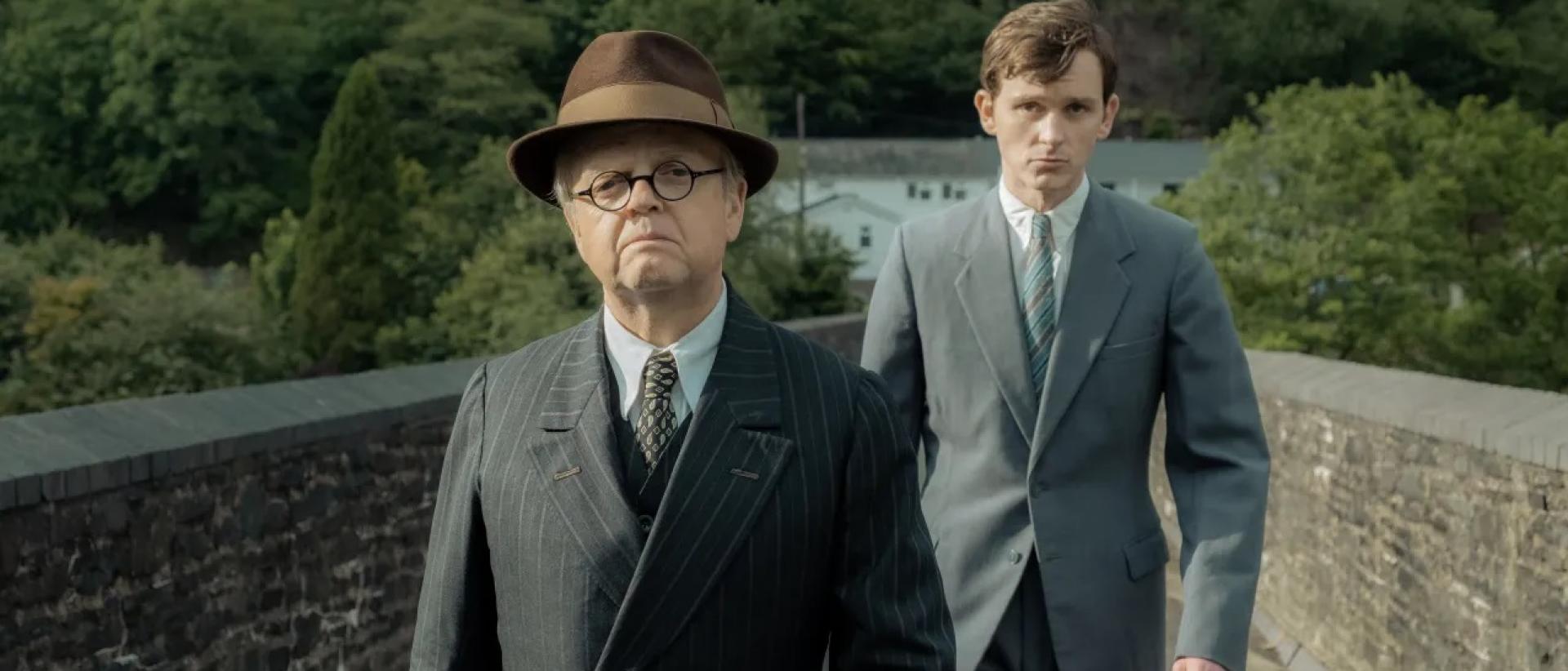 still from mr burton featuring two men in suits walking across a stone brudge