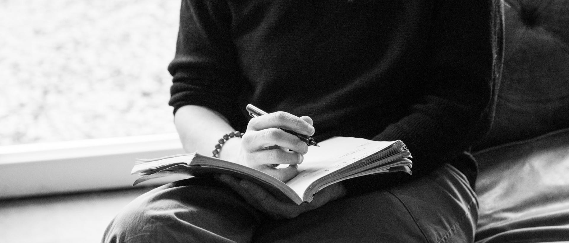 black and white photo of someone writing in a notebook