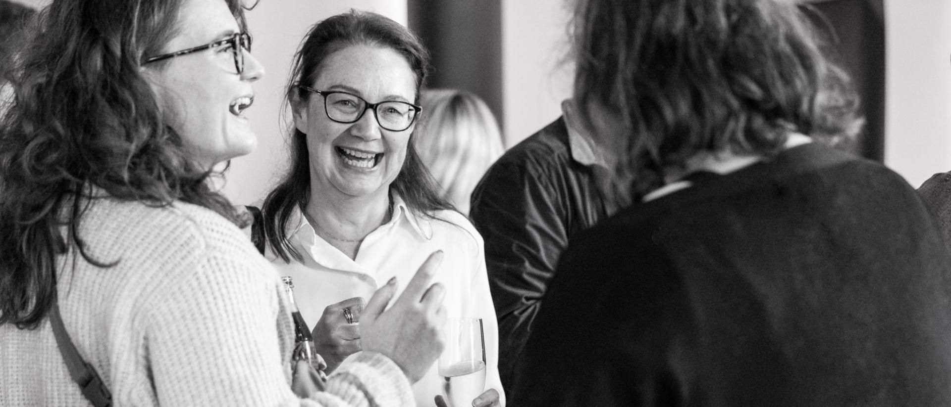 black and white photo of ruth mcelroy at a networking event, holding a glass and laughing