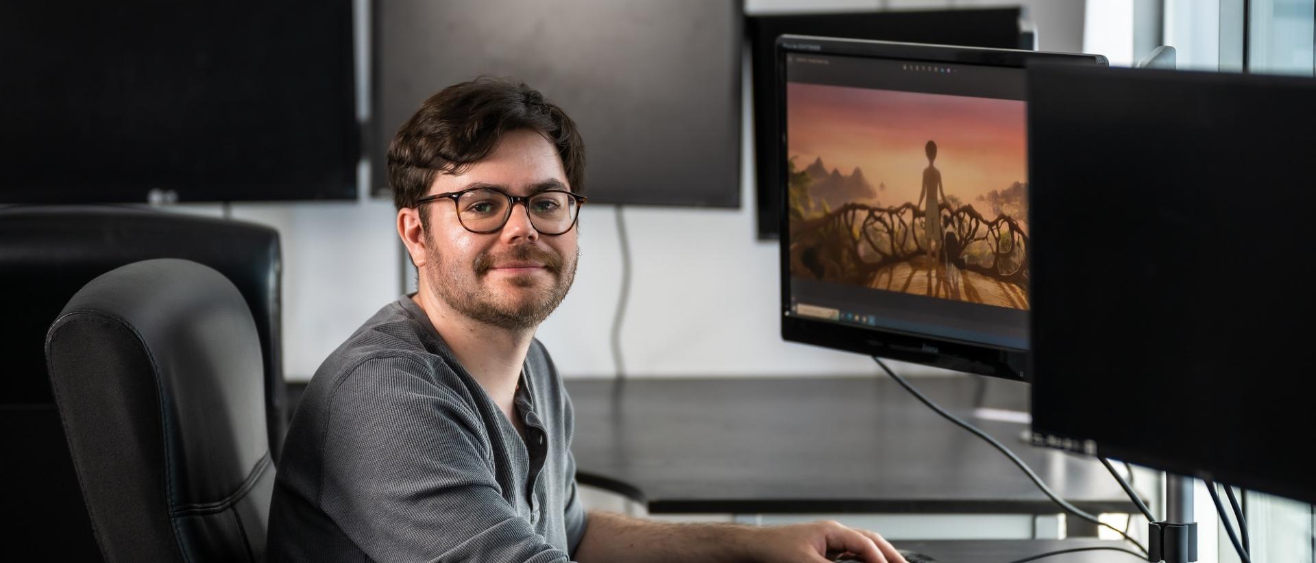 photo of sam wright sitting at a desk with a computer monitor in front of him. On the monitor screen is a still from animated film kensuke's kingdom.