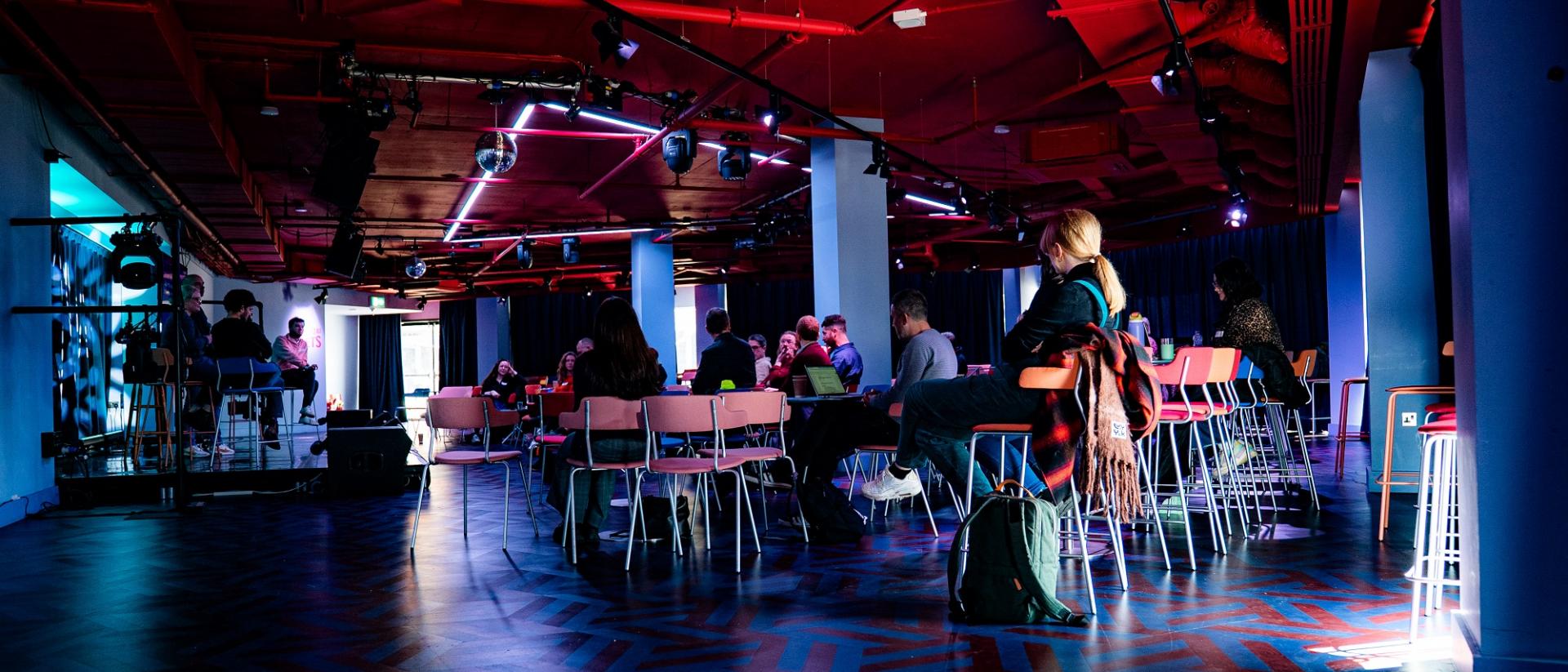 Photo of a cabaret style room with people sitting and watching a panel discussion taking place on stage.