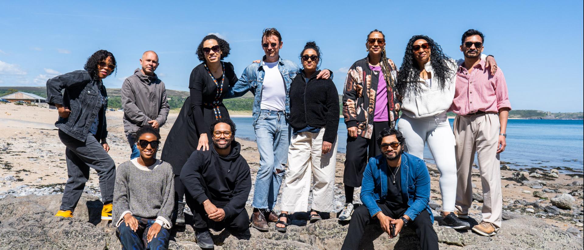 11 people posing for a photo on a rocky coastline with the sea behind them