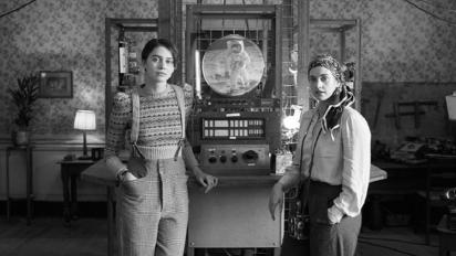 a black and white still from LOLA featuring two women standing in front of a fantastic machine