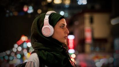 a young woman wearing a hijab and headphones walks through New York at night