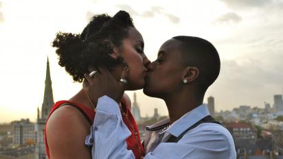 a still from queerama featuring two people kissing on a roof overlooking a city