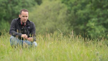 lee haven jones on the set of Gwledd / The Feast crouching in a field of long grass