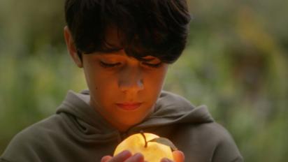 still from the golden apple featuring a young boy holding a glowing golden apple up to his face