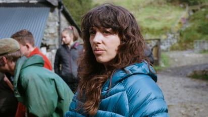a person wearing a thick blue coat standing in a farmyard with three people behind her