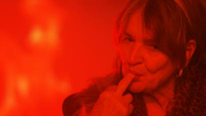 a woman under red light with the end of her middle finger in her mouth,