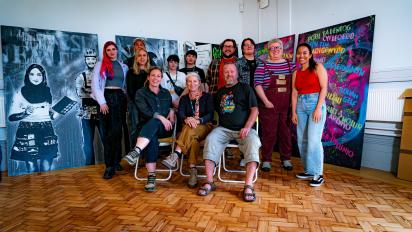 12 people posing for a photo in front of a mural. three are sitting in chairs at the front