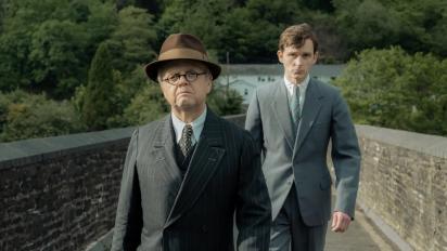 still from mr burton featuring two men in suits walking across a stone brudge