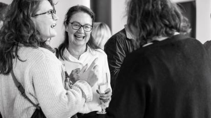 black and white photo of ruth mcelroy at a networking event, holding a glass and laughing