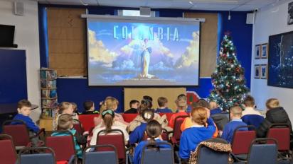 photo of children in blue school uniforms watching a film at a pop-up community cinema. The Columbia logo is on the projector screen and there is a Christmas tree to its right.