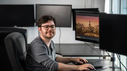 photo of sam wright sitting at a desk with a computer monitor in front of him. On the monitor screen is a still from animated film kensuke's kingdom.