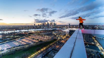 still from documentary film off the rails featuring a person in an orange jacket standing on a high structure looking over london